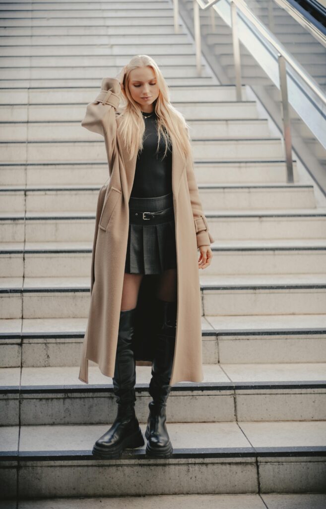 femme chic portant une jupe en cuir, des bottes hautes et un long manteau